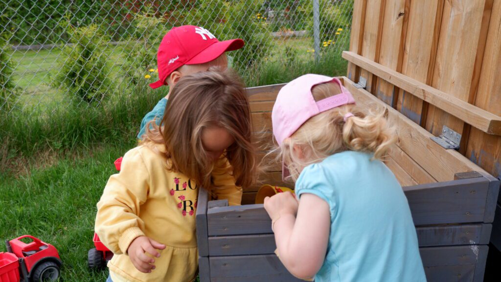 bildet viser tre små barn som ser oppi ei trekasse med leker